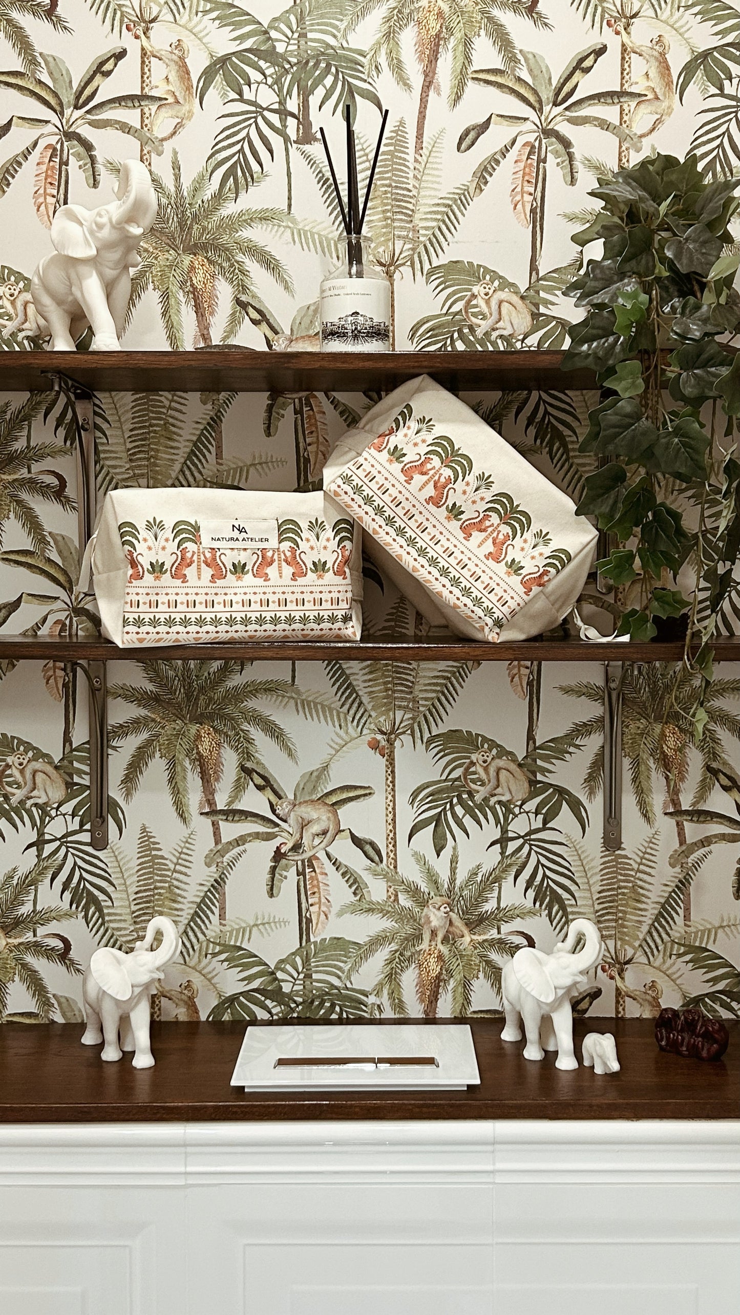Decorative shelf  in the downstairs loo with cotton wash bags and small sculptures against a tropical wallpaper background