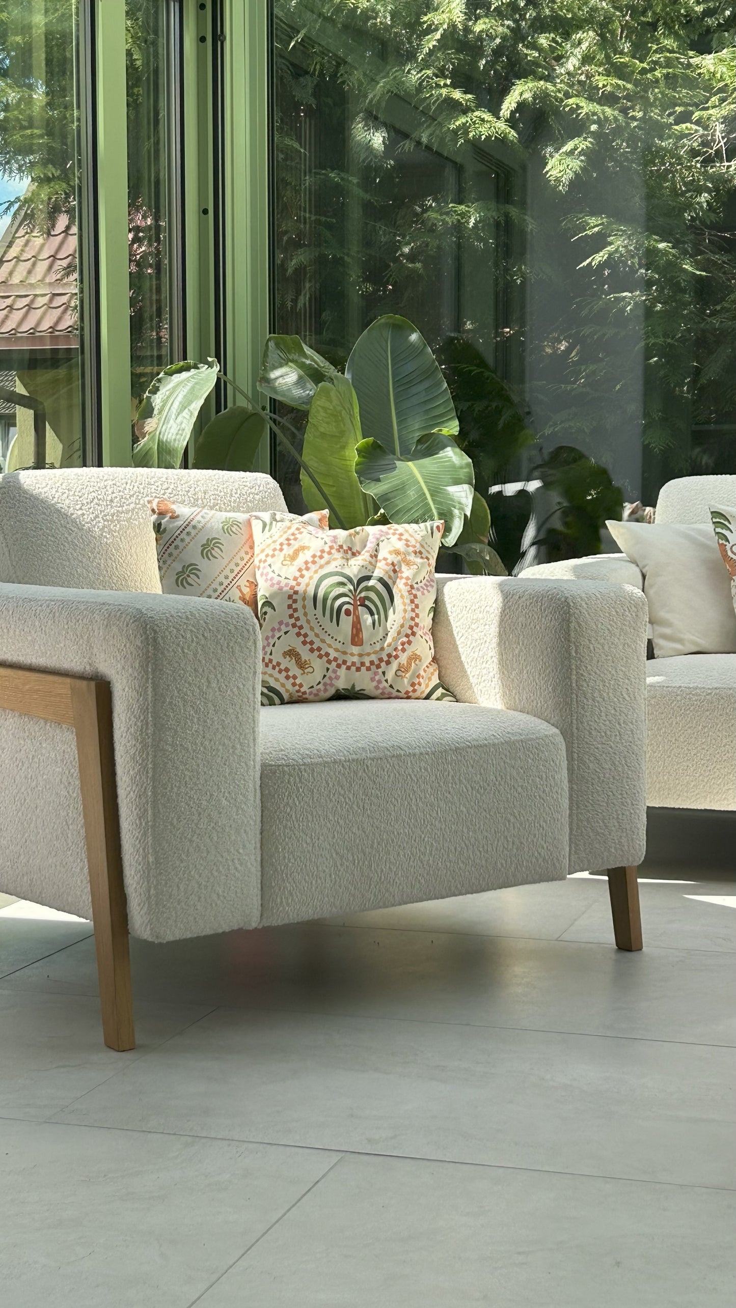 White boucle armchair with decorative cushions in a winter garden with greenery in the background