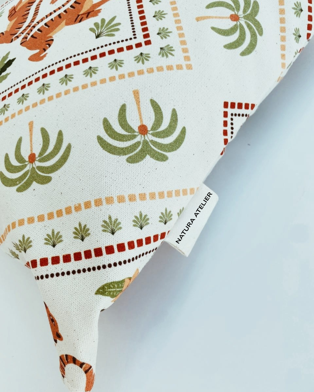 Fabric with a pattern of tigers, plants, and geometric shapes, featuring a NAtura Atelier brand tag