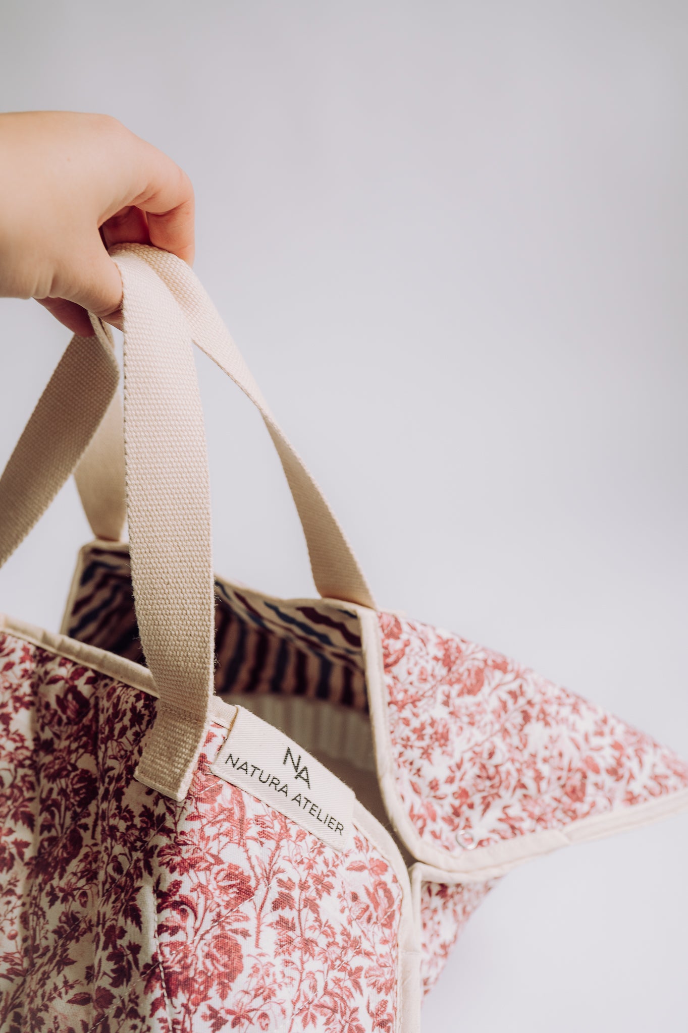 Floral tote bag with a visible brand logo held by a hand against a light background
